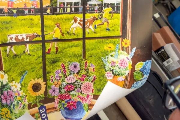 A fresh print of the 2026 fair poster, bouquets in the window and calves in the field beyond