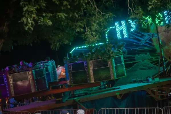 Carnival cars glow green beneath the oaks between rounds