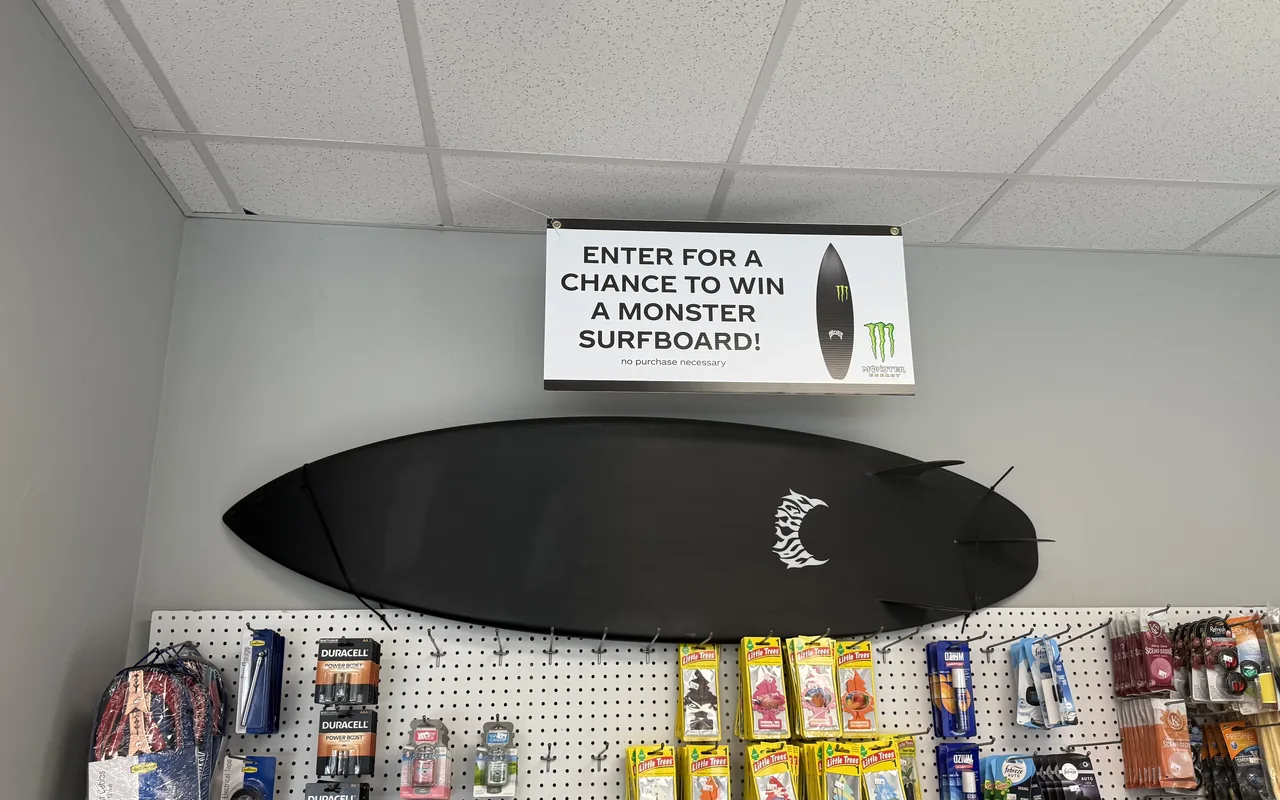 Inside the airport service station shop with a surfboard raffle display above the shelves