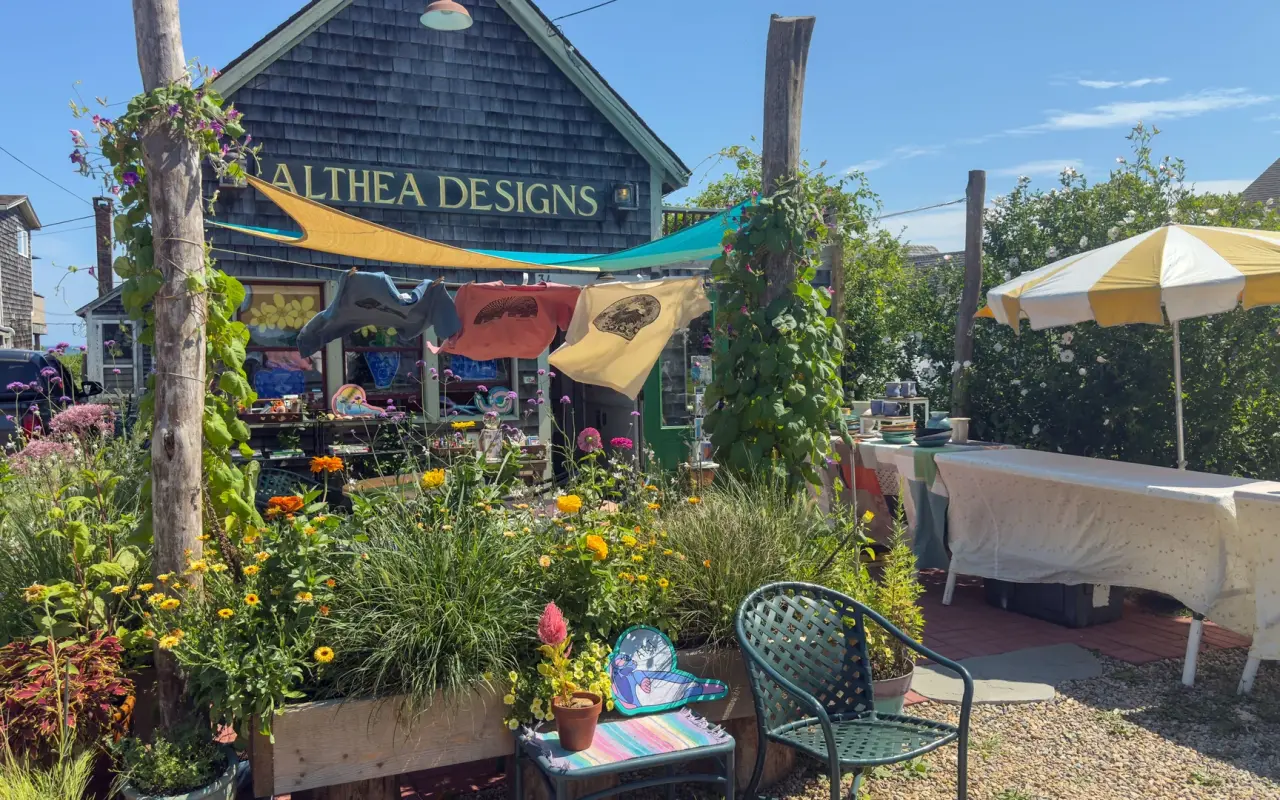 A shingled storefront with the sign Althea Designs, potted flowers and a yellow umbrella on the sidewalk
