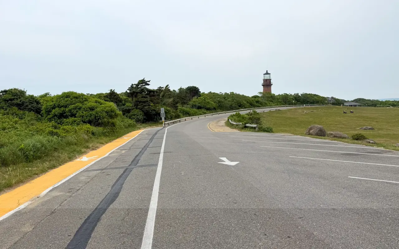 Road curving toward the red brick Gay Head Lighthouse under a pale sky