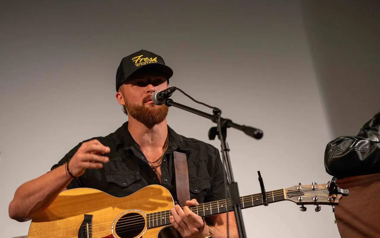 Austin G in a black cap at a microphone with an acoustic guitar