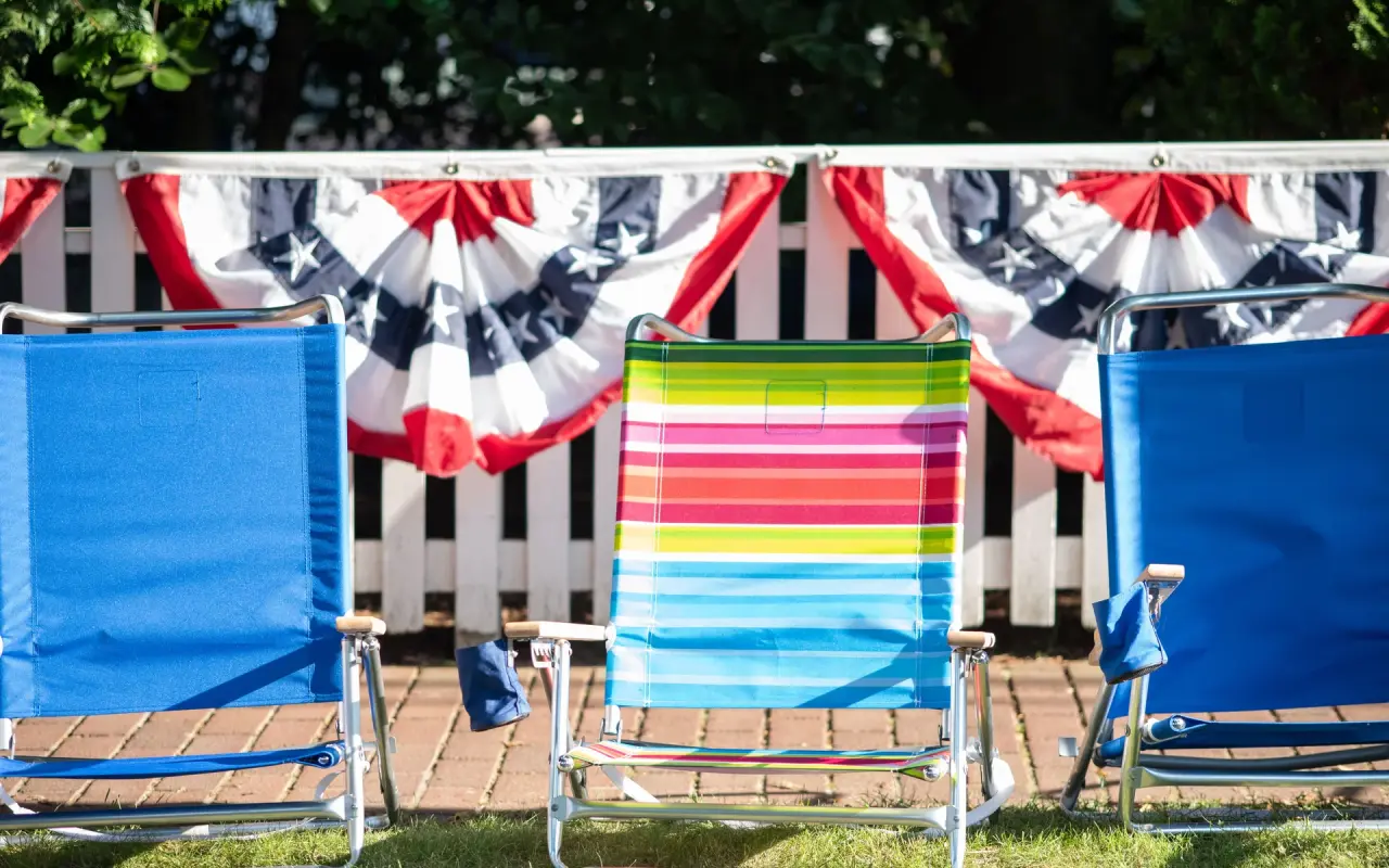 Empty beach chairs saving spots along a patriotic fence before the Edgartown Fourth of July parade