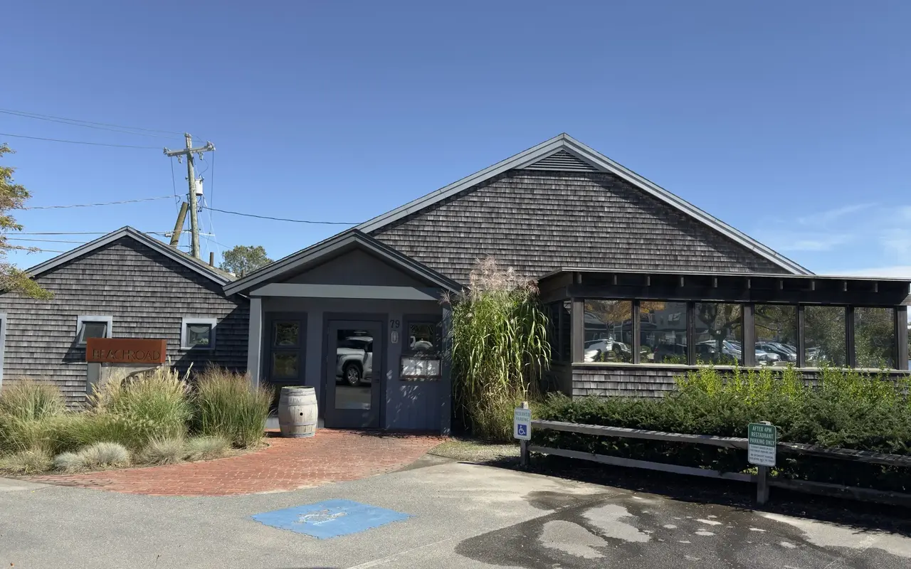 The shingled Beach Road restaurant at 79 Beach Road in Vineyard Haven, with its rust-colored sign, a wine barrel by the door, a glassed-in porch, a reserved accessible space and a green sign on the fence reading After 4PM Restaurant Parking Only
