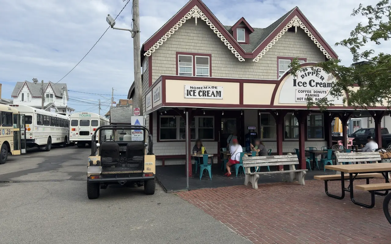 Big Dipper ice cream and coffee stand in Oak Bluffs with people at outdoor tables under the porch and island tour buses parked behind