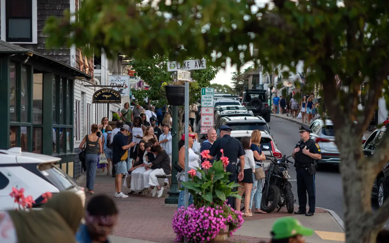 A crowded sidewalk on Circuit Avenue in Oak Bluffs on a summer afternoon with flower planters and parked cars