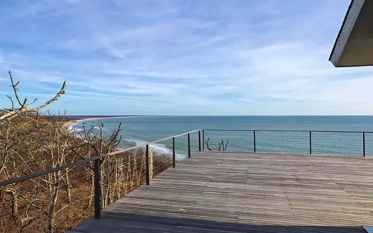 Wooden deck with a railing overlooking a long beach and the open ocean in Chilmark