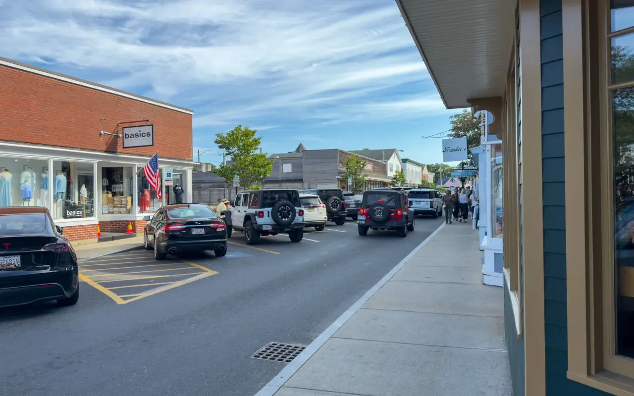 A busy Circuit Avenue in Oak Bluffs in summer with parked cars, shop awnings and people on the sidewalk