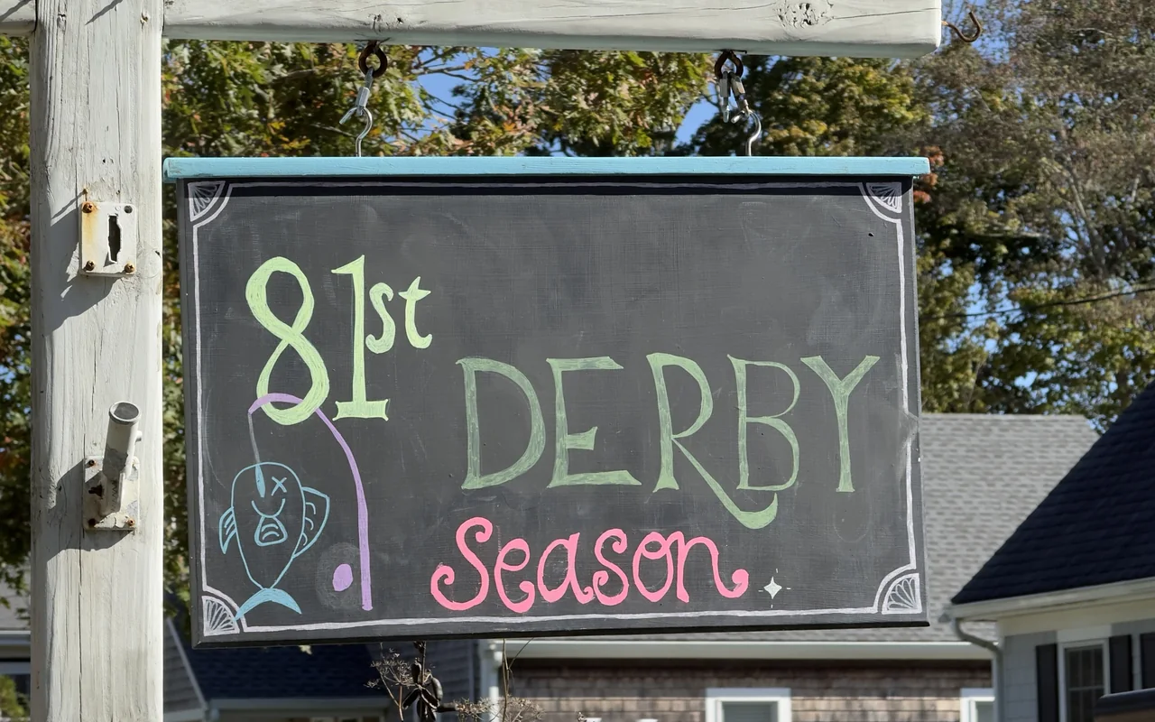 Chalkboard sign reading 81st Derby Season with a drawing of a hooked fish, hanging from a wooden post