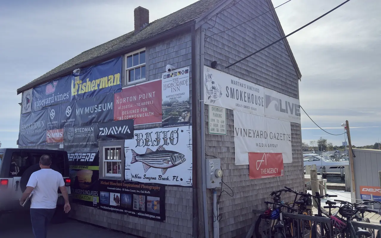 Side wall of the shingled Derby headquarters in Edgartown covered with sponsor banners, bicycles parked by the railing