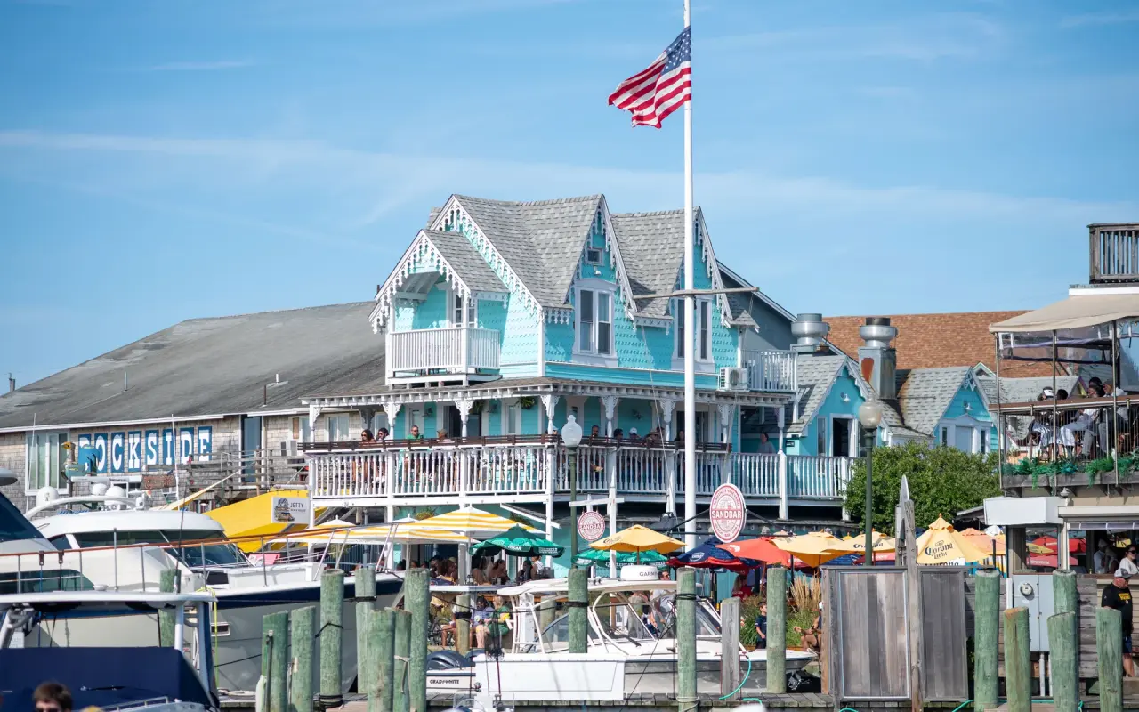 Turquoise gingerbread-trimmed buildings with balconies and umbrellas along the Oak Bluffs harbor with a flag flying