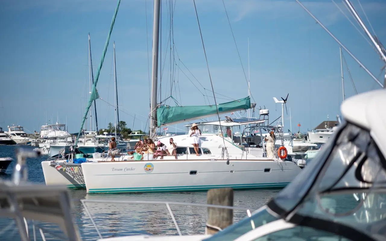 White catamaran with passengers motoring out of Oak Bluffs Harbor among moored boats