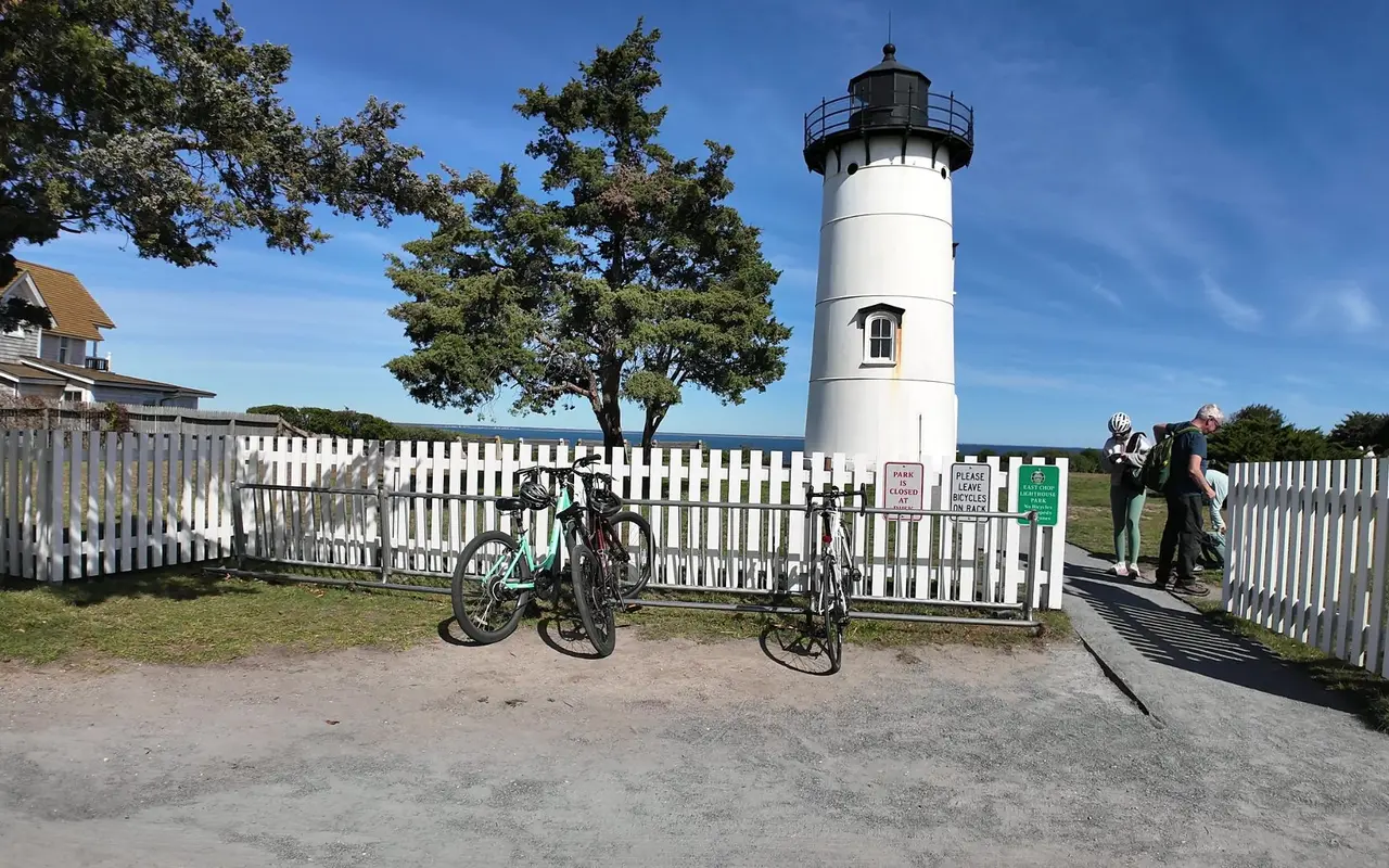 Bicycles parked at a metal rack in front of the white picket fence around East Chop Lighthouse, with signs asking riders to leave bicycles on the rack