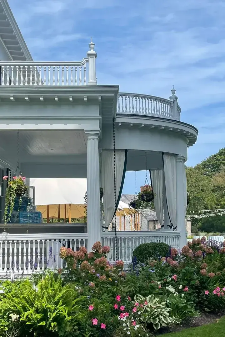 Curved white columned portico of the Dr. Daniel Fisher House in Edgartown with flowers in bloom below