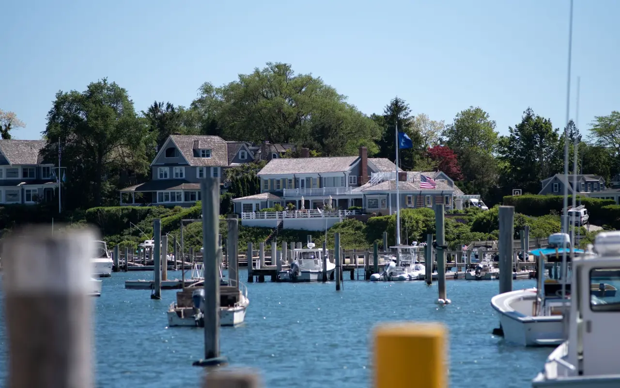 Boats on moorings in Edgartown Harbor with large shingled houses on the far shore
