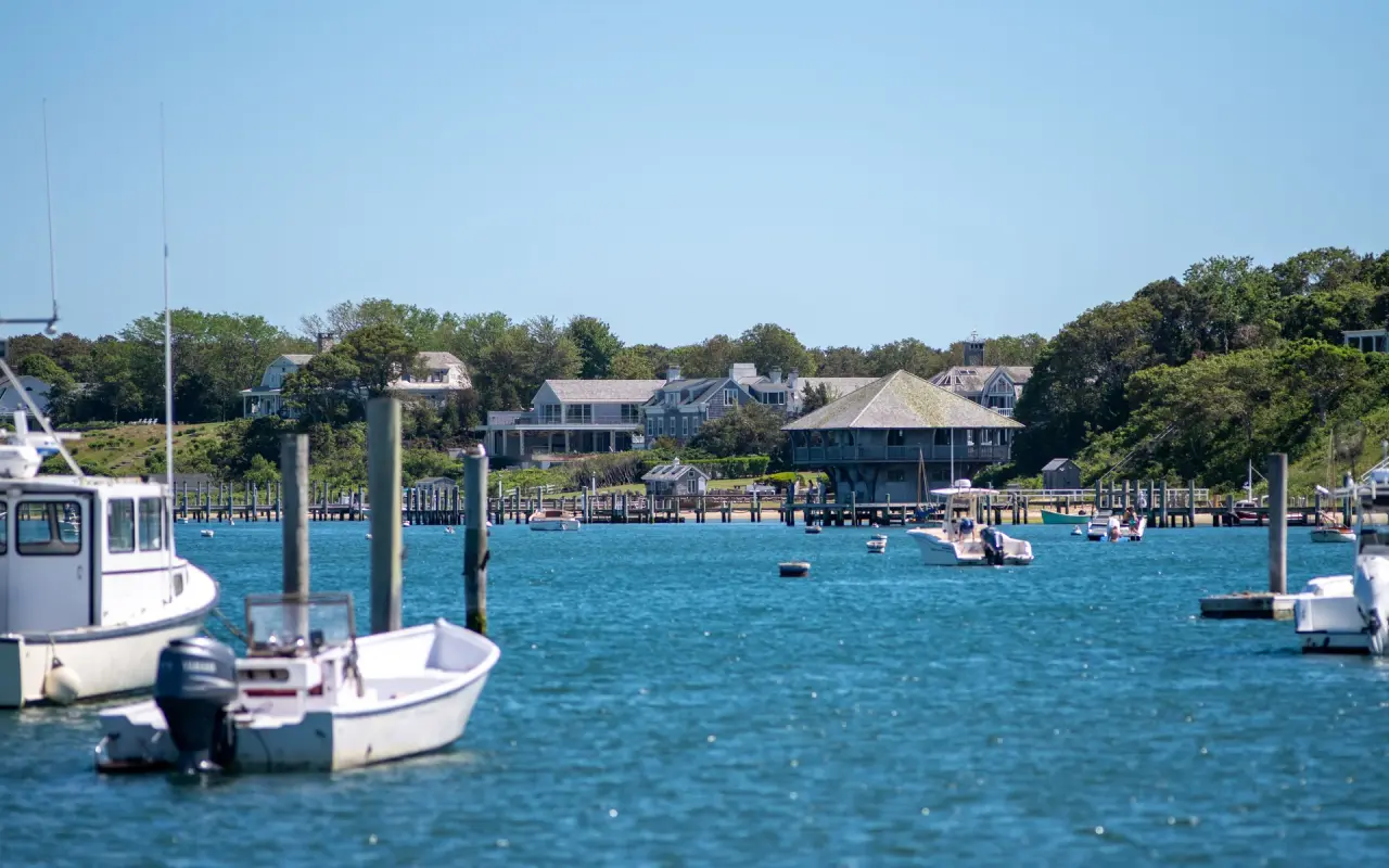Small boats on moorings in Edgartown harbor under a bright blue sky with houses on the far shore