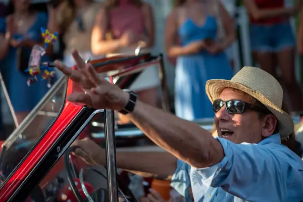 A smiling parade driver tossing candy from a classic car in the Edgartown Fourth of July parade