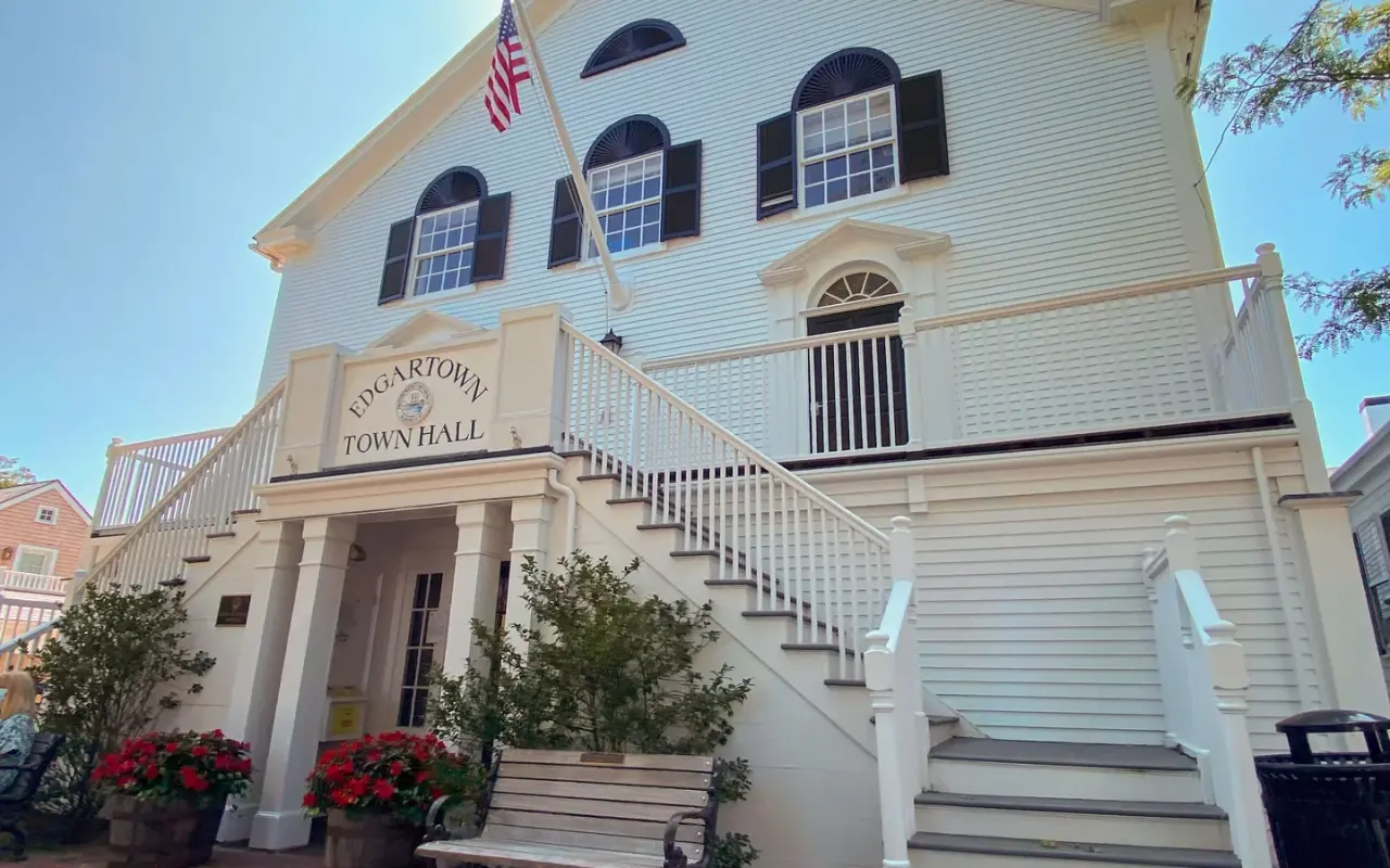 The white clapboard front of Edgartown Town Hall on Main Street with its double staircase, flag and sign