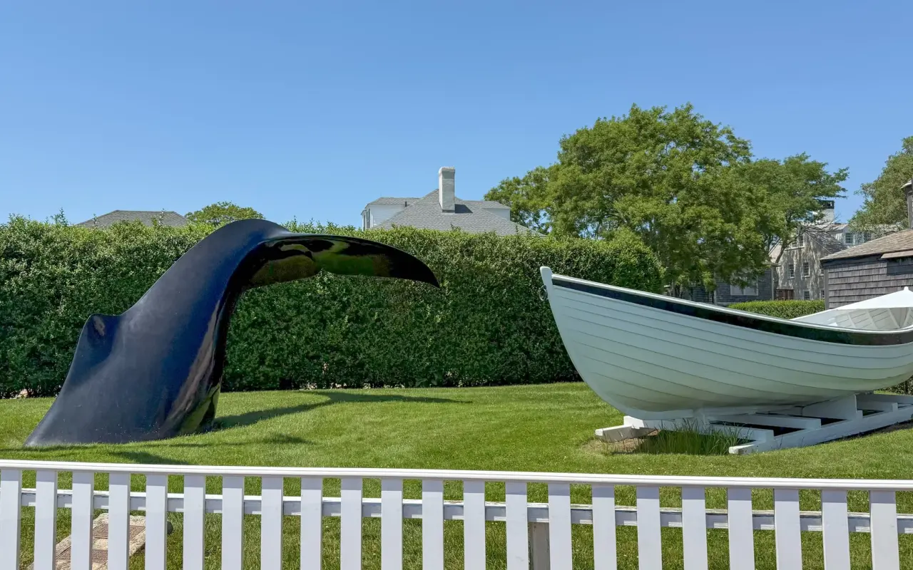 Whale tail sculpture and whaleboat on a lawn in Edgartown