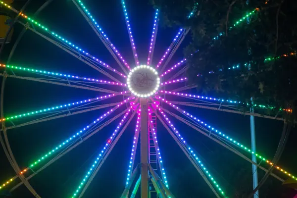 The Ferris wheel hub spins rainbow spokes against the night sky