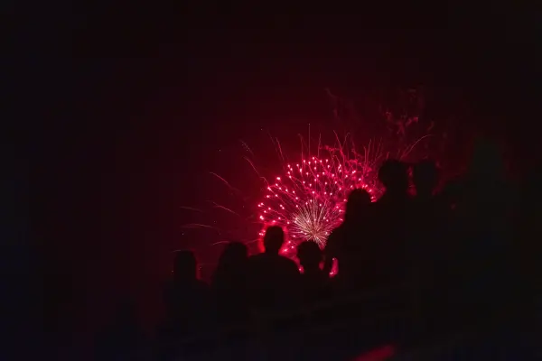 A red firework silhouetting the crowd along the water in Edgartown