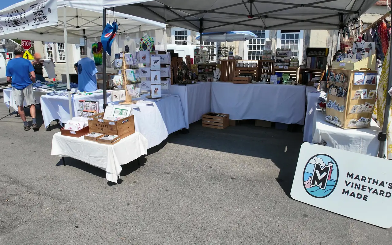 Vendor tables with cards, prints, mugs and T-shirts under white tents, a Martha's Vineyard Made sign leaning in front