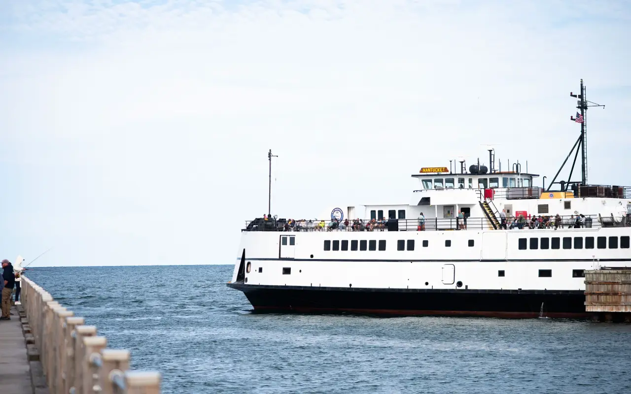White and black Steamship Authority ferry Nantucket approaching a wooden wharf, a fisherman on the jetty at left