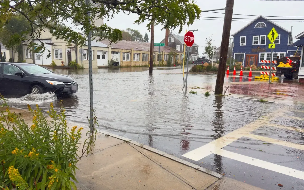 Floodwater across Five Corners in Vineyard Haven on September 26, 2026, a car pushing a wake past a stop sign, sandbags by the Vineyard Grill