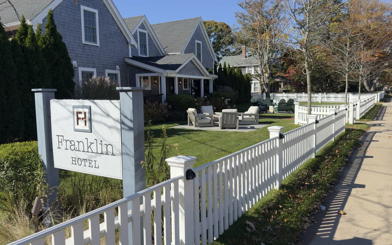 Grey-shingled Franklin Hotel in Edgartown behind a white picket fence, with its sign and outdoor chairs on the lawn