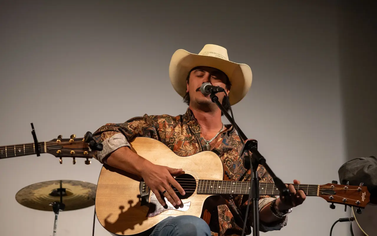 Fuller in a straw cowboy hat playing an acoustic guitar at a microphone