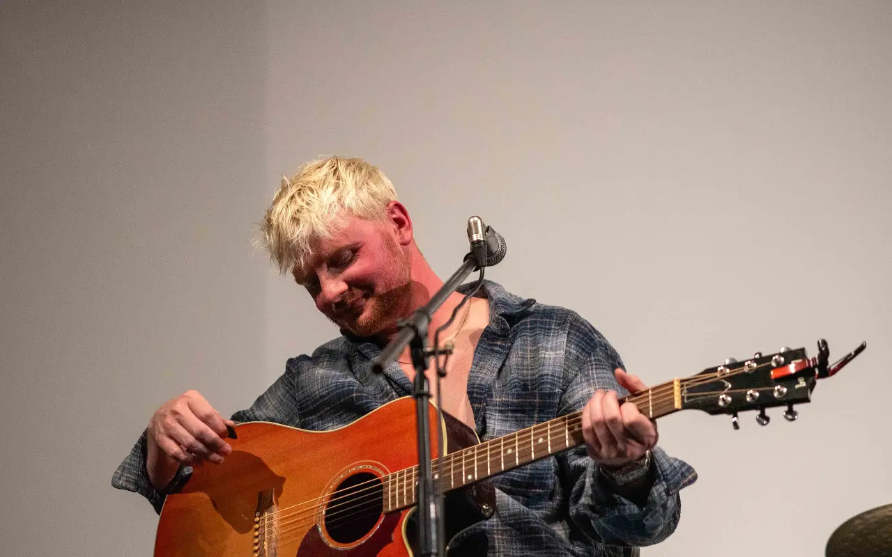 Garrett Owens looking down at his acoustic guitar on the Strand stage