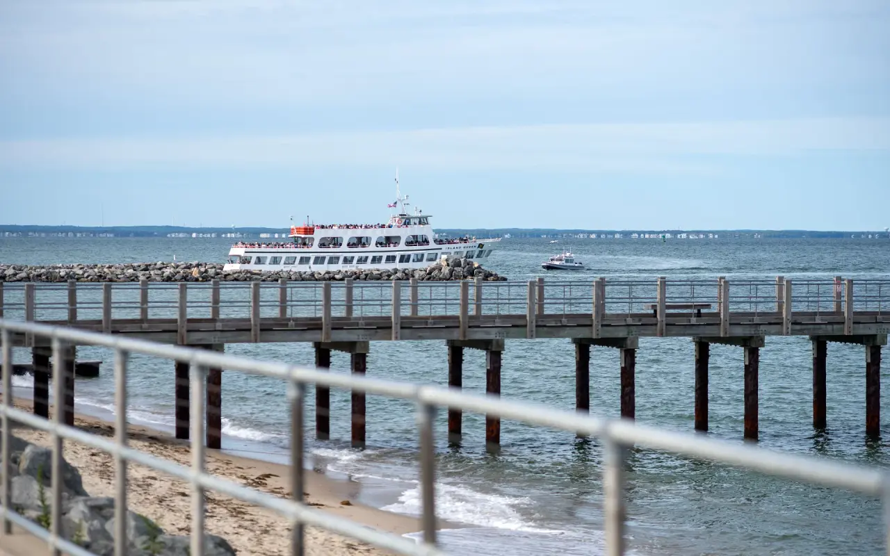 Island Queen passenger ferry passing a rock jetty behind a wooden fishing pier