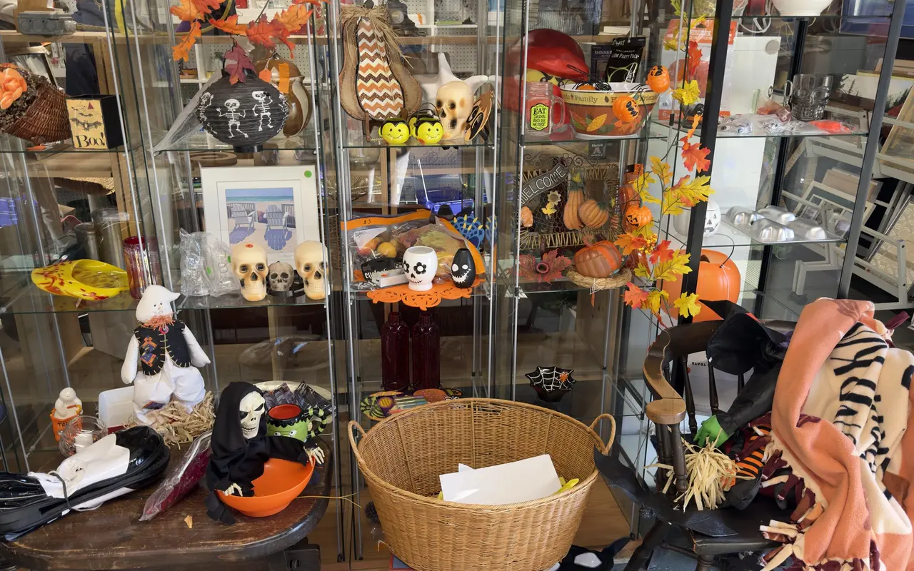 Glass display cases at the Chicken Alley Thrift Shop in Vineyard Haven filled with Halloween decorations: skull candles, a skeleton paper lantern, a grim reaper candy bowl, a stuffed ghost and fall leaf garlands