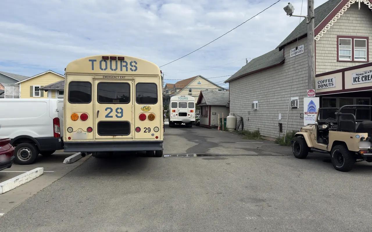 Two cream-colored island tour buses parked in an Oak Bluffs lot beside a shingled building with coffee, donuts and ice cream signs