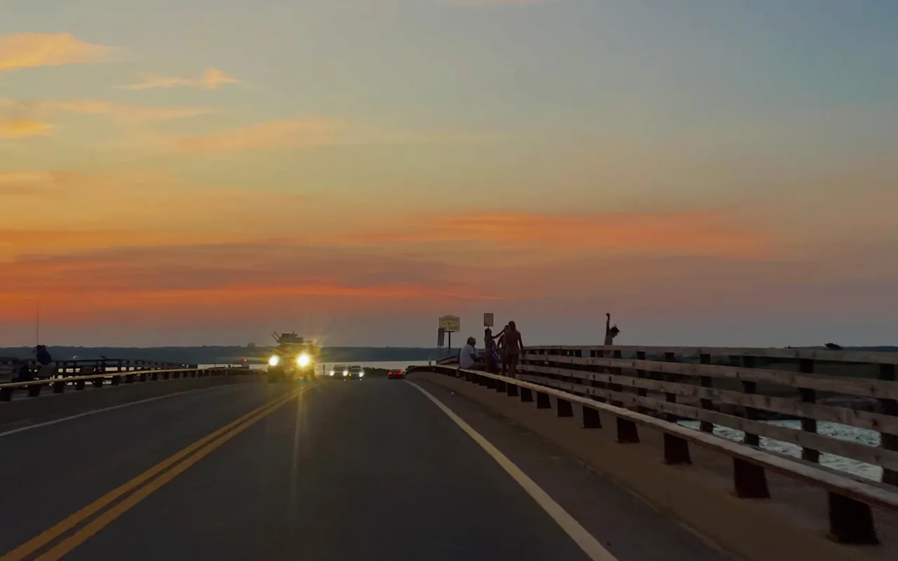 The Jaws Bridge on Beach Road at sunset with headlights approaching and a figure jumping from the rail