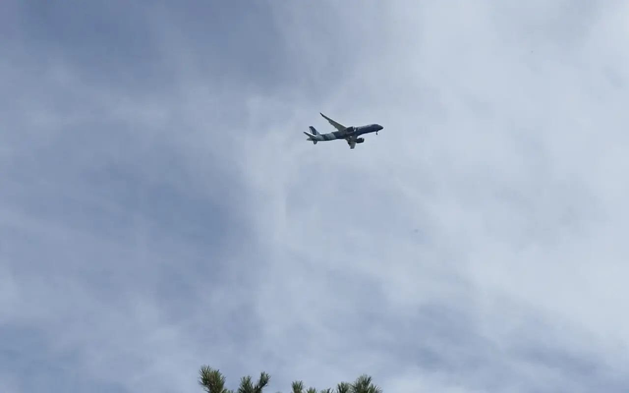 A passenger jet flying low over oaks and pines on Martha's Vineyard under a hazy blue sky