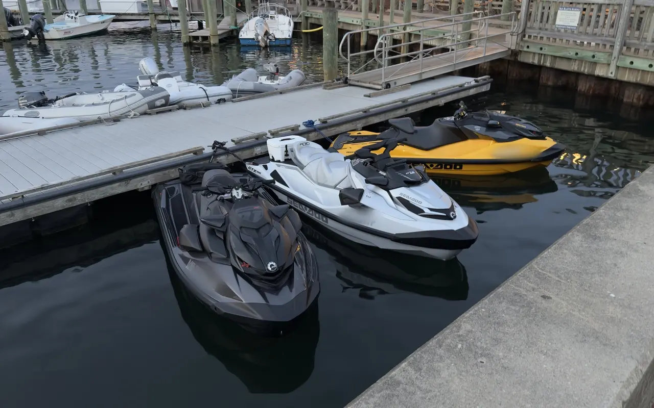 Three Sea-Doo jet skis, black, white and yellow, tied to a floating dock at the Oak Bluffs Marina with inflatable dinghies rafted behind them
