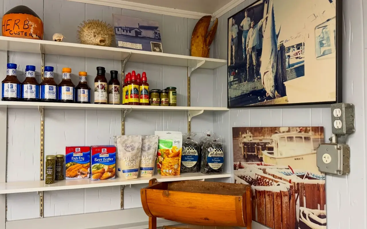 Shelves of sauces and breading mixes beside framed vintage fishing photographs inside a small fish market