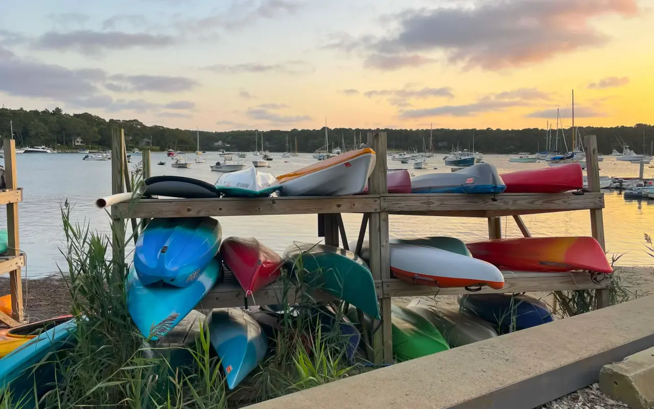 Colorful kayaks on a wooden rack beside Lake Tashmoo at sunset