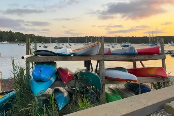 Colorful kayaks racked beside Lake Tashmoo at sunset