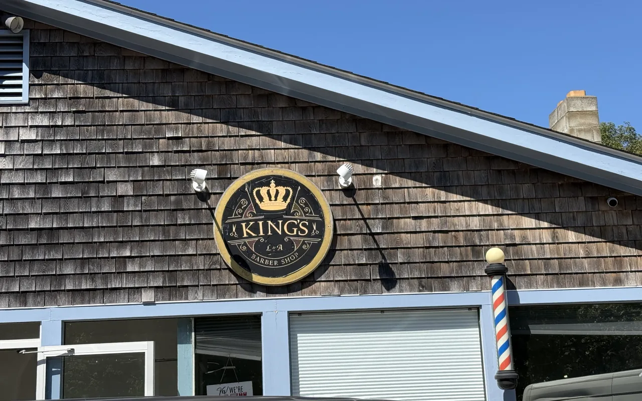 The round King's Barber Shop sign and a striped barber pole on a shingled storefront in Vineyard Haven