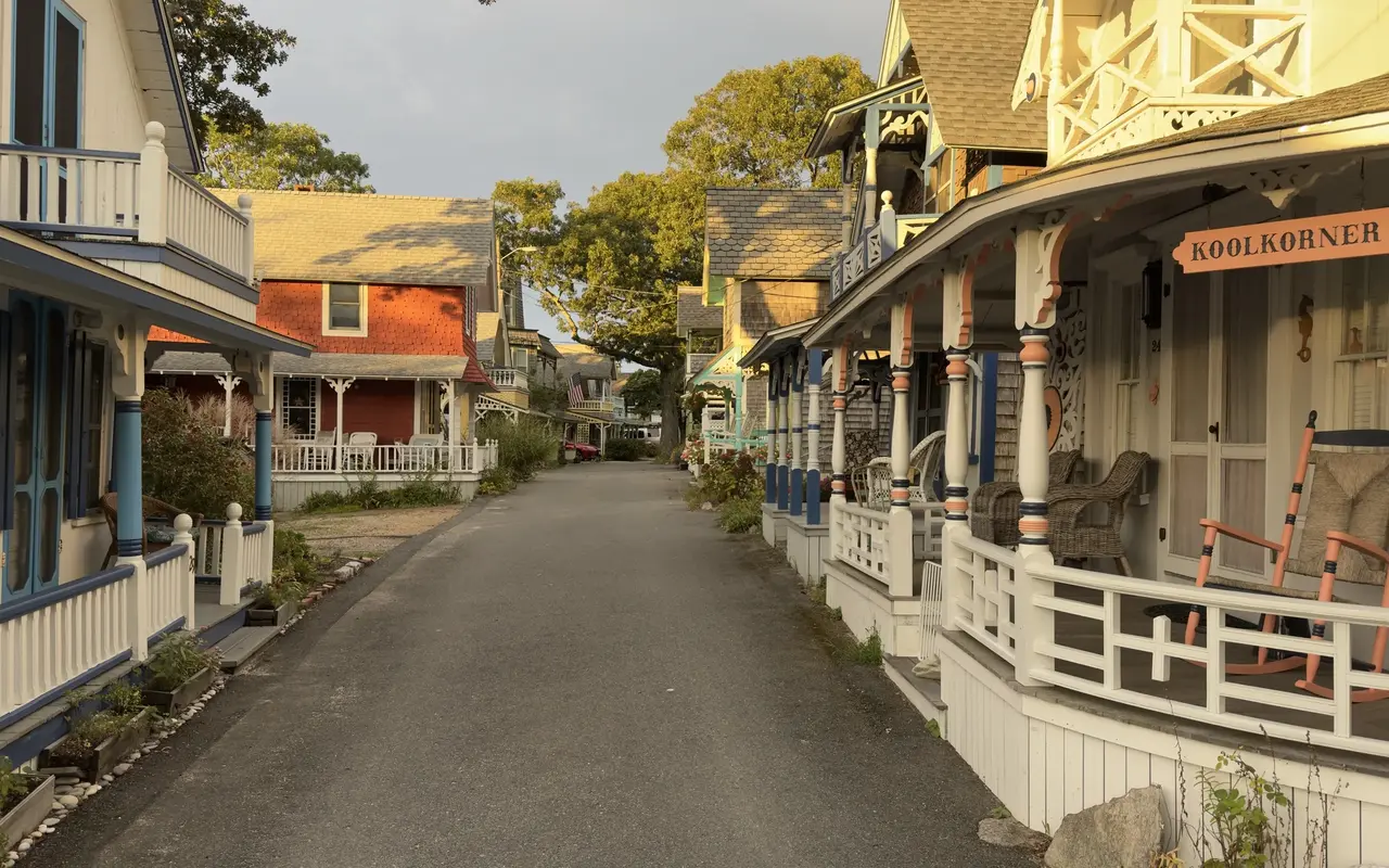 A Campground lane in Oak Bluffs at golden hour: the Koolkorner cottage porch with orange rockers on the right, a red cottage and a row of porches down the lane