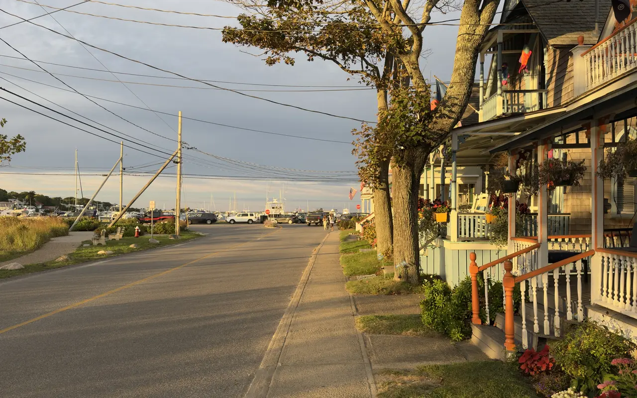 Gingerbread cottage porches with orange trim along Lake Avenue in Oak Bluffs at golden hour, the harbor masts at the end of the street