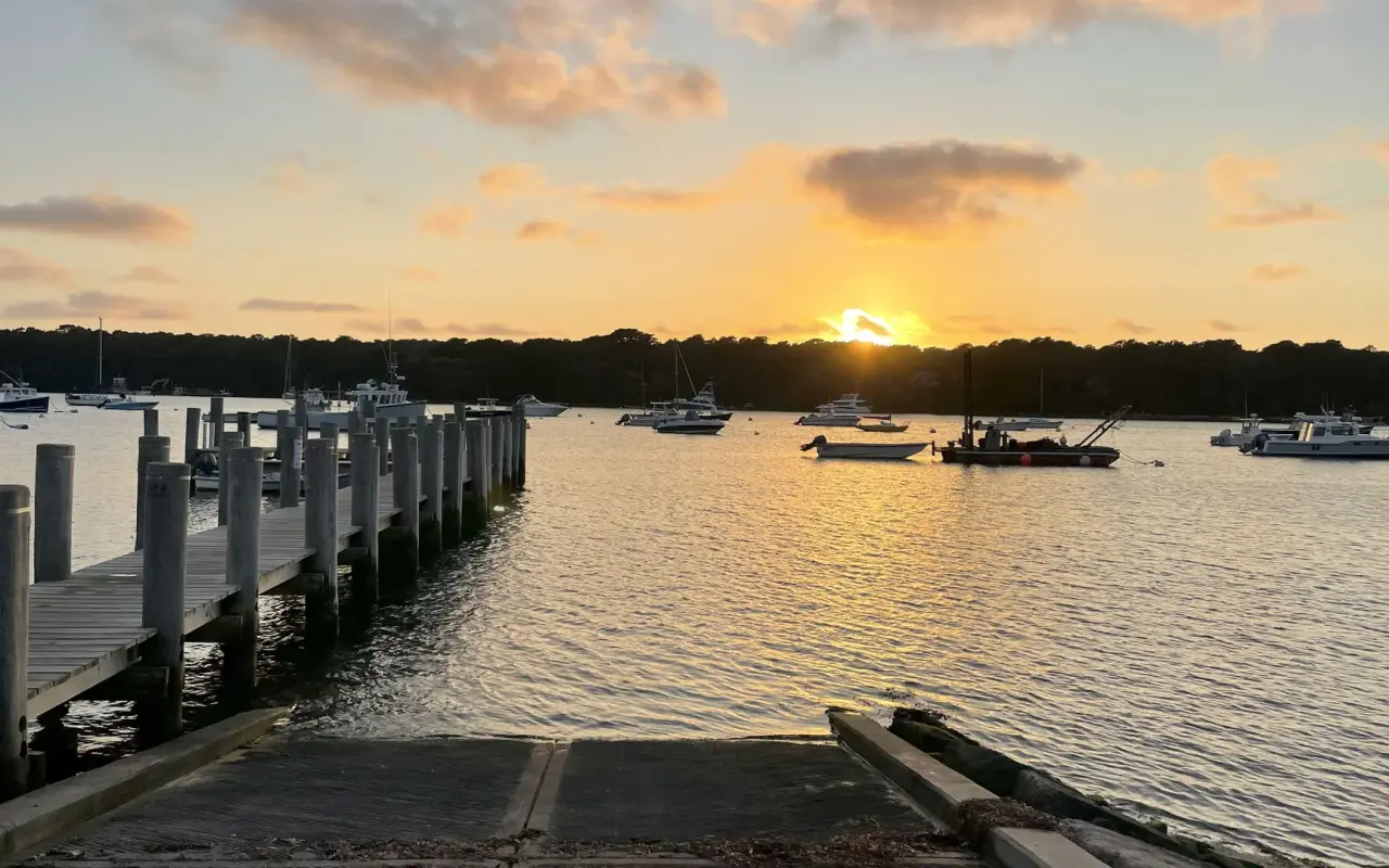 Concrete boat ramp and wooden dock pilings at Lake Street Landing on Lake Tashmoo at sunset, moored boats behind