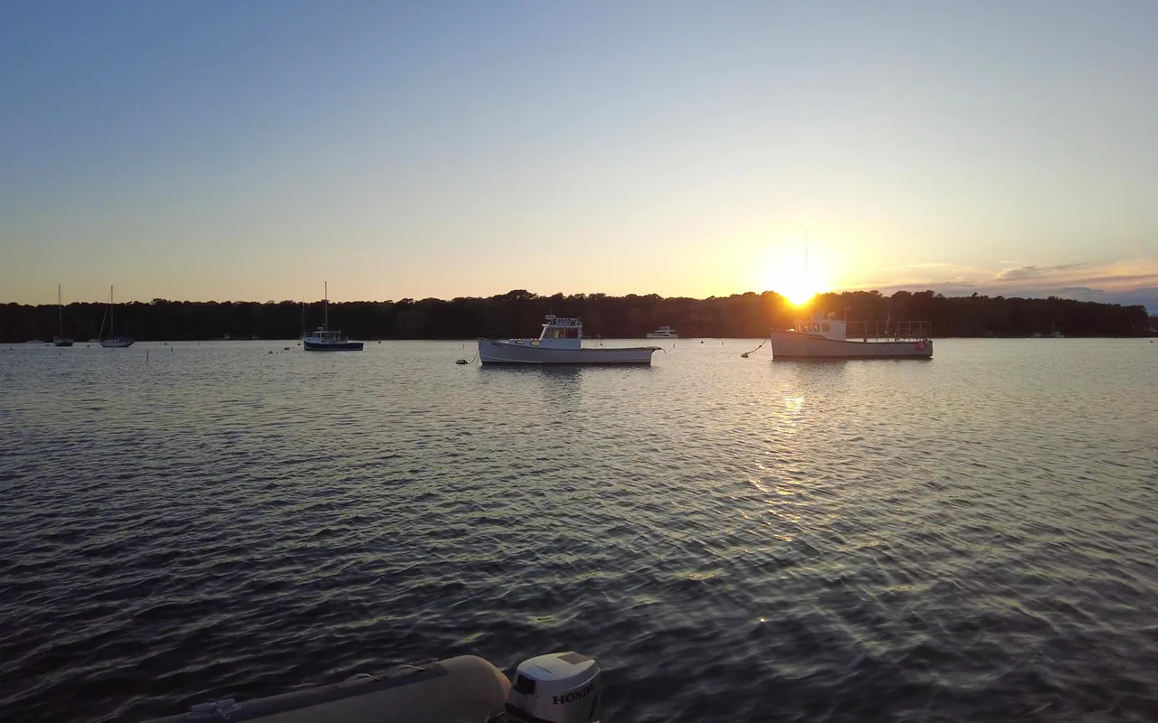 Sun setting behind a wooded shore with a few moored boats on calm water
