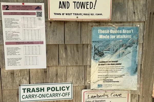 The sign wall at the Lambert's Cove entrance: towing, Route 2 bus, dunes, trash, season dates.