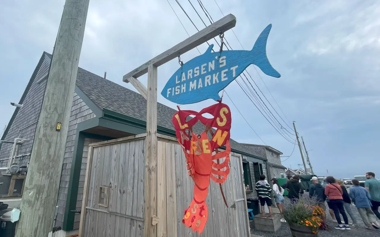 Carved fish sign and painted lobster banner outside Larsen’s Fish Market in Menemsha