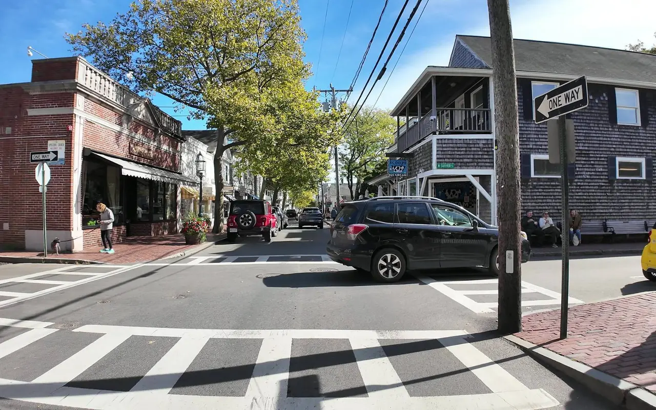 The corner of Main Street and North Summer Street in Edgartown with a brick building, one-way signs, a crosswalk, an ice cream shop with a cow sign and people on a bench