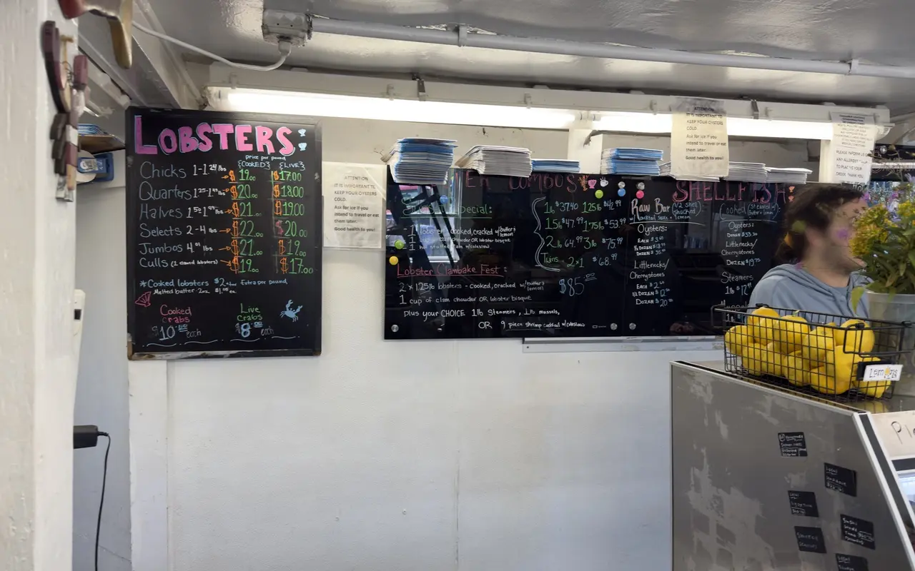 Chalkboard lobster price list by size, cooked and live, beside a combo and raw bar board and a basket of lemons at Menemsha Fish Market