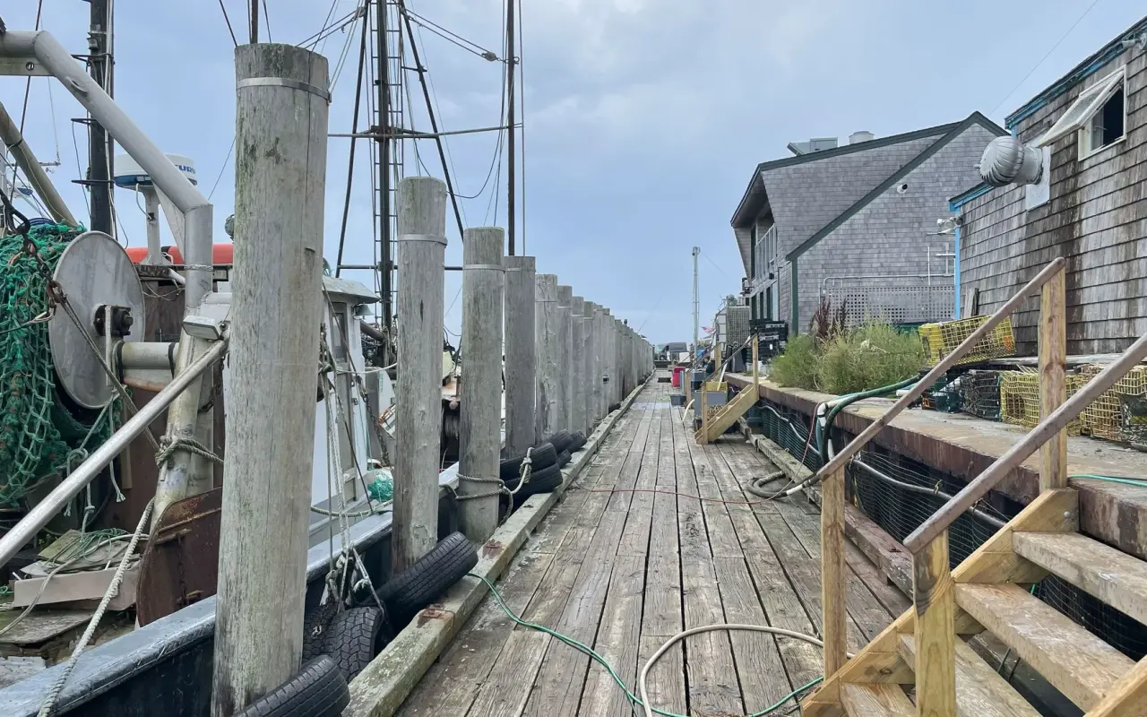 Wooden dock with tall pilings and a fishing boat beside weathered fish houses in Menemsha